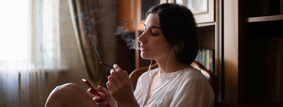 woman sitting at the chair at home, listen to the music and smoking a joint
