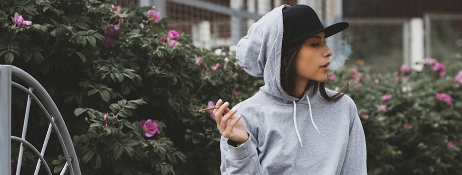 woman with hoodie, cap, jeans smoking a joint outside in Canada.